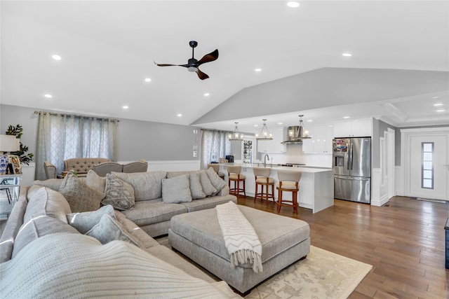 living room featuring ceiling fan with notable chandelier, lofted ceiling, sink, and light hardwood / wood-style flooring