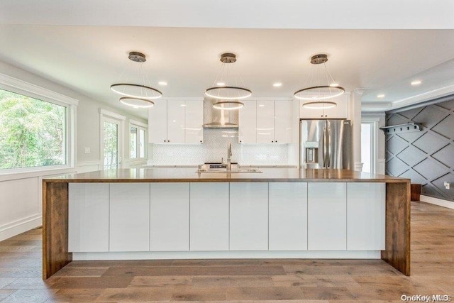 kitchen with white cabinetry, decorative light fixtures, stainless steel fridge with ice dispenser, and wall chimney range hood