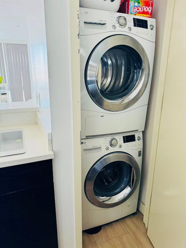 laundry room featuring stacked washing maching and dryer, sink, and light wood-type flooring