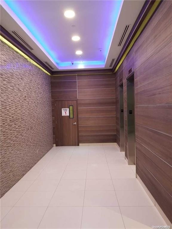 hall with light tile patterned floors and a tray ceiling