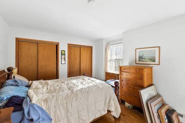 bedroom featuring baseboard heating, hardwood / wood-style floors, and two closets