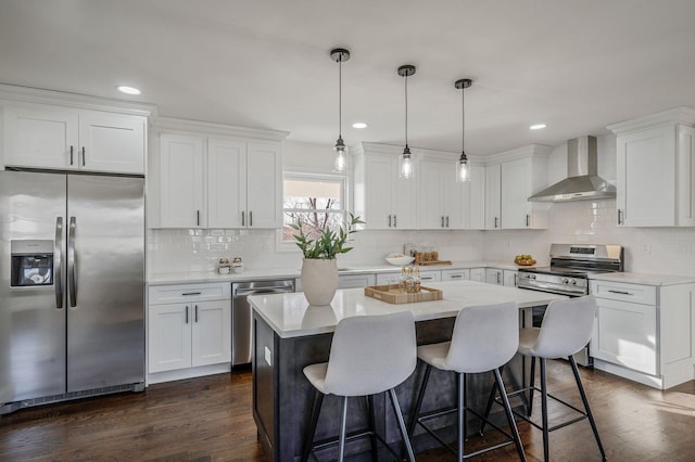 kitchen featuring wall chimney exhaust hood, white cabinetry, stainless steel appliances, and decorative light fixtures