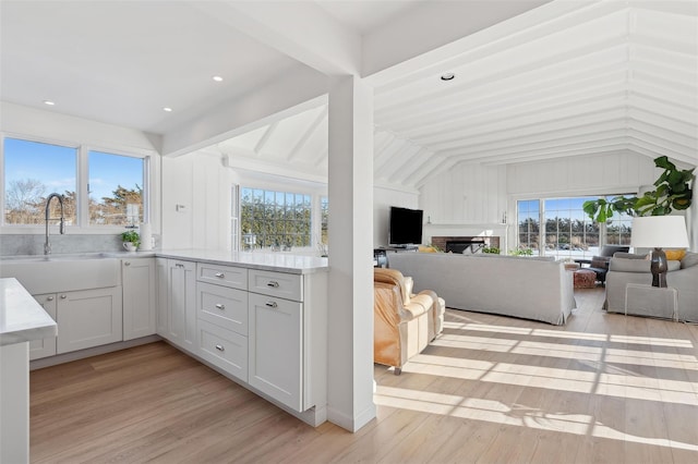 kitchen with lofted ceiling with beams, sink, white cabinets, and light hardwood / wood-style flooring