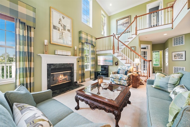 carpeted living area with recessed lighting, a fireplace, a towering ceiling, stairs, and crown molding