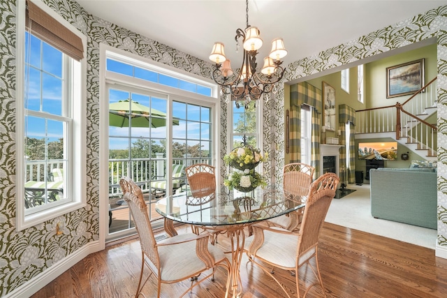 dining area with wallpapered walls, a fireplace, an inviting chandelier, and wood finished floors