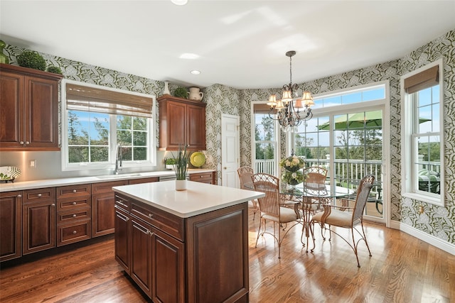 kitchen with wallpapered walls, a kitchen island, decorative light fixtures, light countertops, and a sink