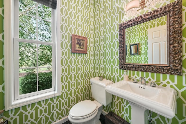 half bath featuring a sink, toilet, and wallpapered walls