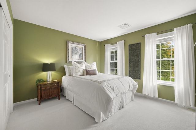 bedroom featuring baseboards, multiple windows, visible vents, and light colored carpet