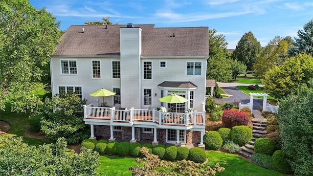 back of house with a yard, a chimney, a shingled roof, a deck, and stone siding