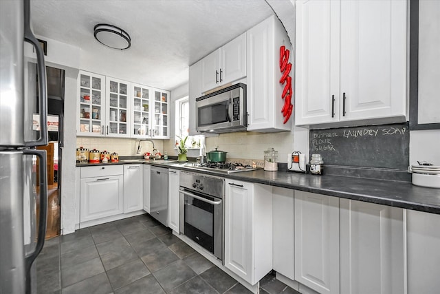 kitchen with tasteful backsplash, white cabinetry, appliances with stainless steel finishes, and dark tile patterned flooring