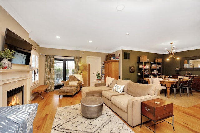 living room featuring an inviting chandelier, crown molding, a fireplace, and light wood-type flooring