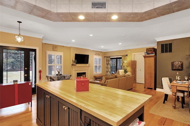 kitchen featuring wood counters, decorative light fixtures, dark brown cabinetry, crown molding, and light hardwood / wood-style flooring