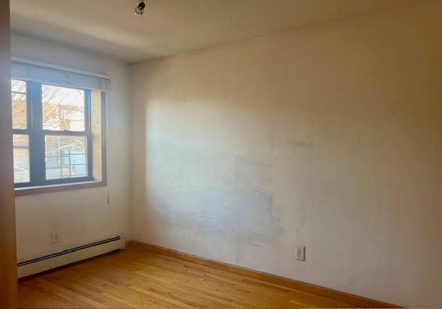 spare room featuring baseboard heating and light hardwood / wood-style flooring