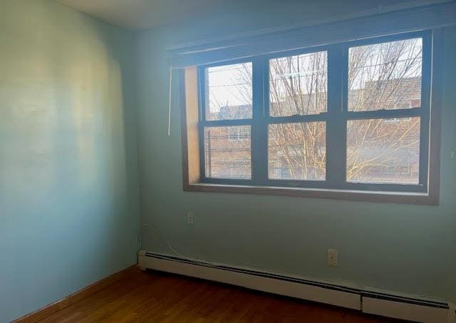 unfurnished room with dark wood-type flooring, a baseboard radiator, and plenty of natural light