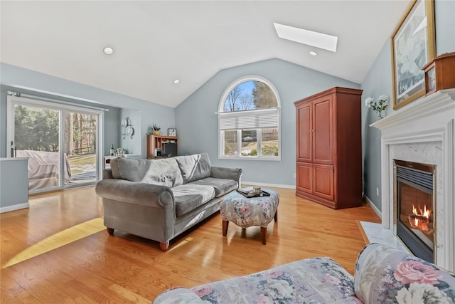 living room featuring a high end fireplace, vaulted ceiling with skylight, and light wood-type flooring