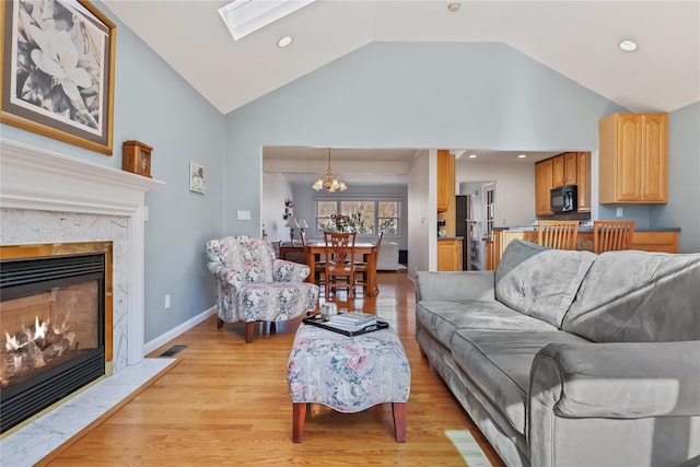 living room with a chandelier, a skylight, high vaulted ceiling, light wood-type flooring, and a fireplace