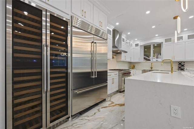 kitchen featuring wall chimney exhaust hood, sink, premium appliances, beverage cooler, and white cabinets