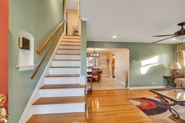 stairs featuring hardwood / wood-style flooring, crown molding, and ceiling fan with notable chandelier