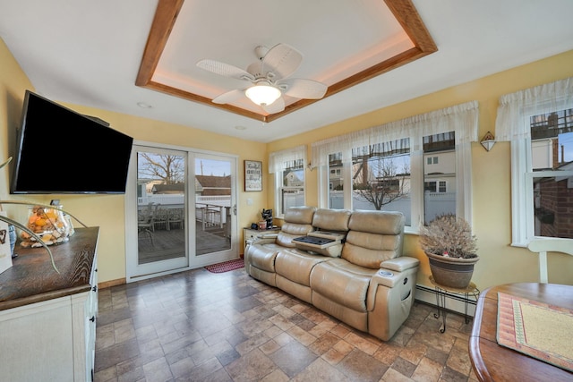 living room with a baseboard heating unit, a raised ceiling, and ceiling fan