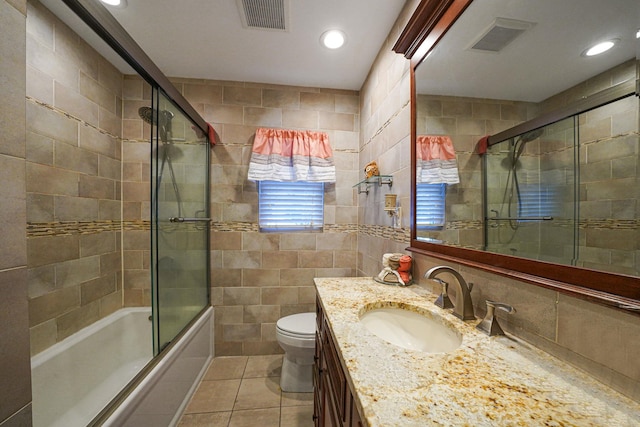 full bathroom with combined bath / shower with glass door, tile walls, tile patterned flooring, vanity, and toilet