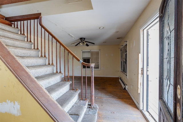 stairs featuring a baseboard heating unit, hardwood / wood-style floors, and ceiling fan