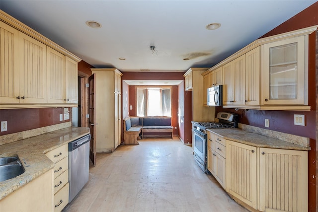 kitchen with light brown cabinetry, sink, light wood-type flooring, stainless steel appliances, and light stone countertops