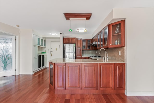 kitchen with pendant lighting, sink, stainless steel fridge, kitchen peninsula, and dark wood-type flooring