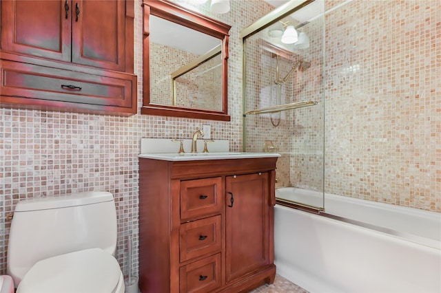 full bathroom featuring bath / shower combo with glass door, vanity, toilet, and tile walls