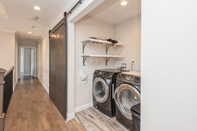 clothes washing area with light hardwood / wood-style flooring, washing machine and dryer, and a barn door