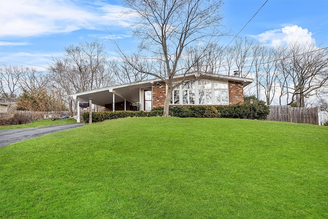 view of front of property featuring driveway, fence, a front lawn, a carport, and brick siding