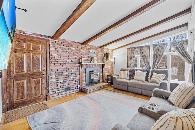 living room featuring brick wall, beamed ceiling, wood finished floors, and a wood stove