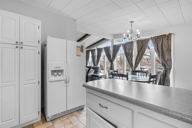 kitchen with white refrigerator with ice dispenser, white cabinets, stone finish floor, decorative light fixtures, and an inviting chandelier