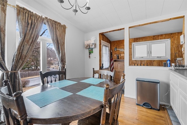 dining area with light wood-style flooring, wooden walls, and a chandelier