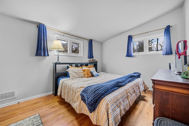 bedroom with lofted ceiling, visible vents, baseboards, and wood finished floors