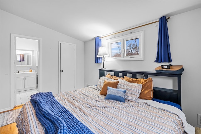 bedroom featuring vaulted ceiling, ensuite bath, and wood finished floors