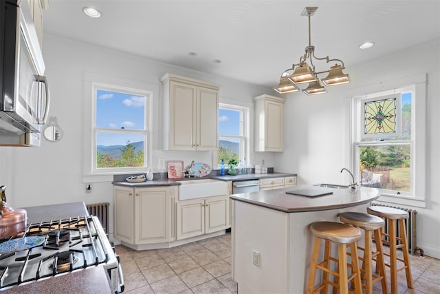 kitchen featuring pendant lighting, sink, stainless steel appliances, cream cabinets, and a center island with sink