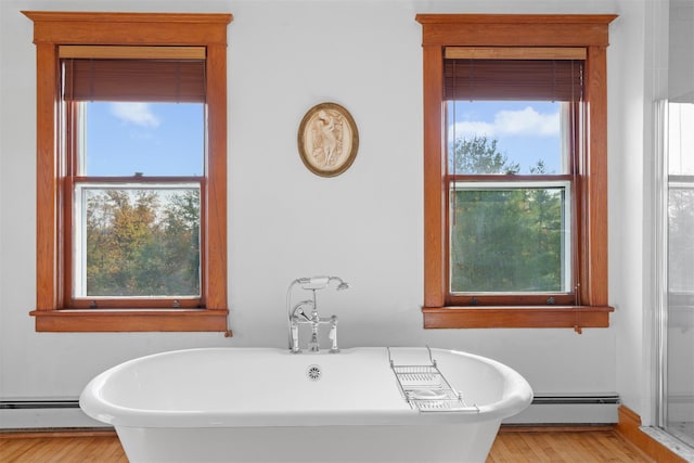 bathroom with a tub to relax in, wood-type flooring, and a baseboard heating unit