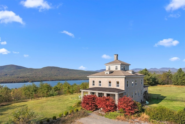 exterior space featuring fence, a chimney, a water and mountain view, and a front yard