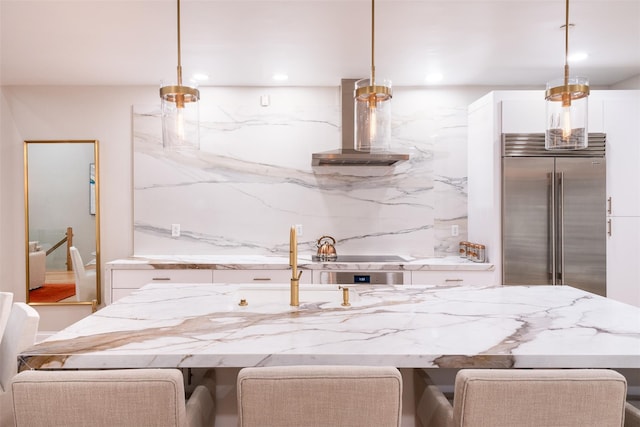 kitchen with wall chimney range hood, a breakfast bar, hanging light fixtures, and stainless steel built in refrigerator