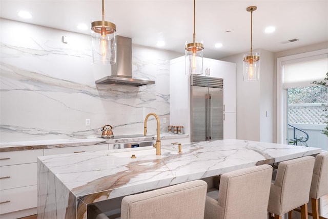 kitchen with pendant lighting, island range hood, white cabinets, and built in refrigerator