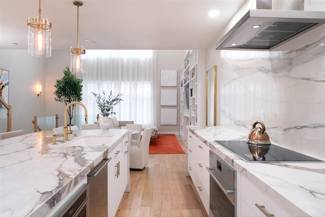 kitchen featuring sink, light stone countertops, white cabinets, island exhaust hood, and decorative light fixtures