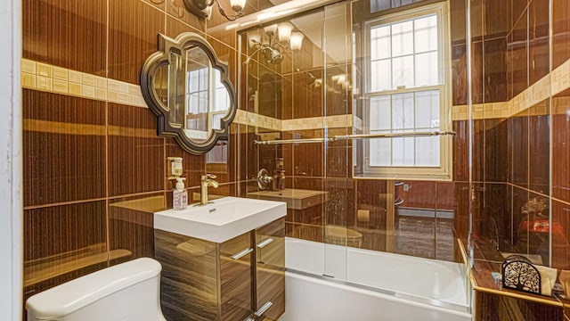 bathroom with toilet, a sink, bath / shower combo with glass door, and tile walls