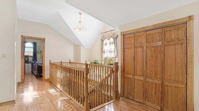 corridor featuring a chandelier, light wood-style flooring, vaulted ceiling, and an upstairs landing