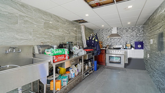 kitchen featuring wall chimney exhaust hood, a drop ceiling, a sink, and dark tile patterned flooring