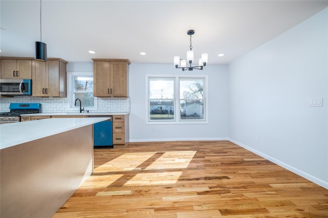 kitchen with sink, light hardwood / wood-style flooring, appliances with stainless steel finishes, hanging light fixtures, and tasteful backsplash