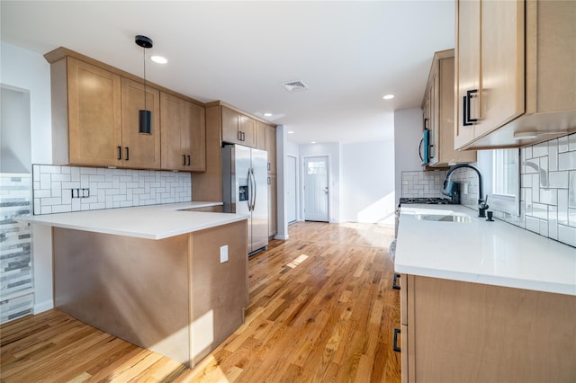 kitchen with appliances with stainless steel finishes, decorative light fixtures, kitchen peninsula, and light wood-type flooring