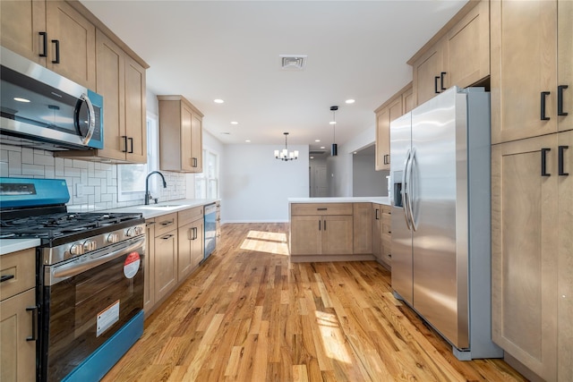 kitchen featuring sink, light hardwood / wood-style flooring, appliances with stainless steel finishes, hanging light fixtures, and decorative backsplash