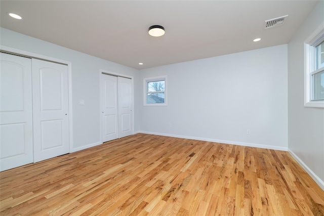 unfurnished bedroom with multiple closets and light wood-type flooring