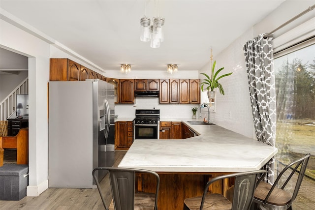 kitchen with sink, gas stove, stainless steel fridge with ice dispenser, kitchen peninsula, and light wood-type flooring