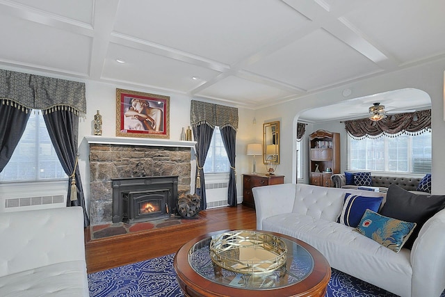 living area featuring arched walkways, coffered ceiling, a fireplace, and wood finished floors